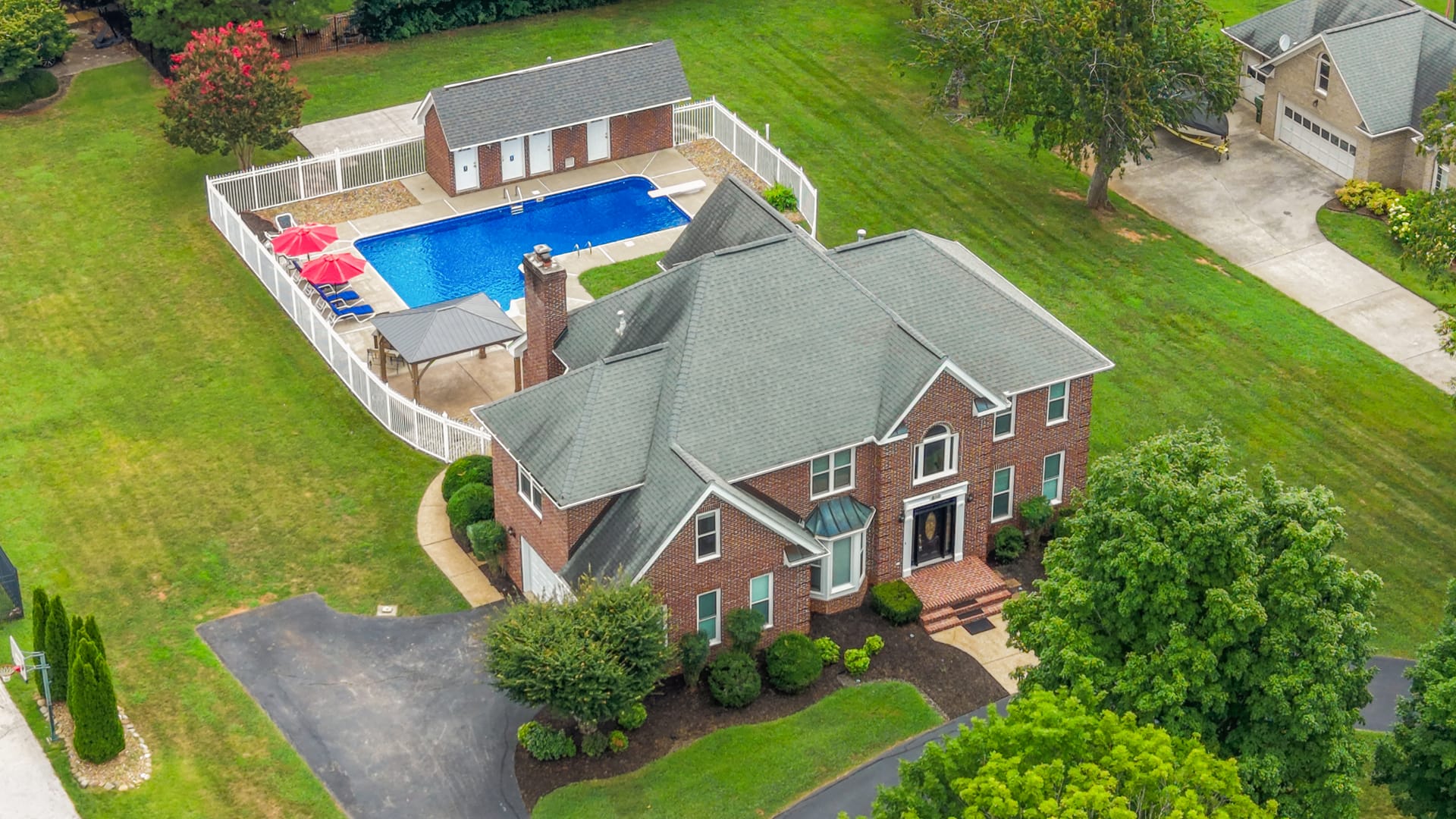 Aerial drone photo of a brick estate with a fenced pool and gazebo